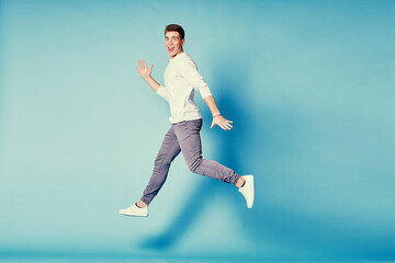 Fototapeta premium Colorful studio portrait of happy young man dancing jumping against blue background.