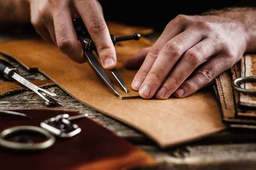 Deurstickers Close up of a shoemaker or artisan worker hands. Leather craft tools on old wood table. Leather craft workshop. © mathefoto