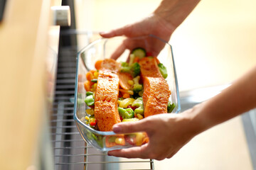culinary, food and people concept - woman cooking salmon fish with vegetables in baking dish in...