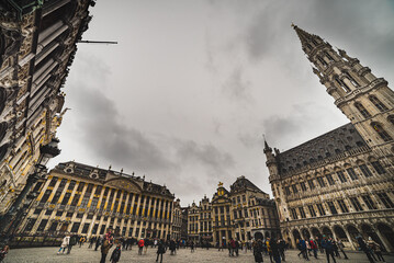 People in the historical Grand Place with the City Hall tower rising in the scene. People walk on the cobbled Grand Square amid Gothic and Baroque architecture - Brussels, Belgium