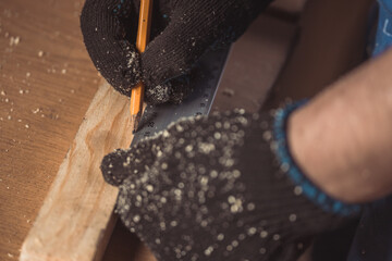 Close-up The man measures a wooden board with a ruler and marks with pencil the necessary points...