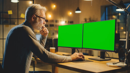 Creative Middle Aged Designer Sitting at His Desk Uses Desktop Computer with Two Green Mock-up...