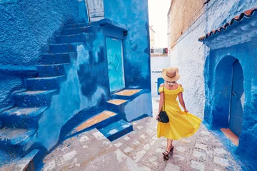 Deurstickers Kleurrijk reizen door Marokko. Jonge vrouw in gele jurk wandelen in de medina van de blauwe stad Chefchaouen. © luengo_ua
