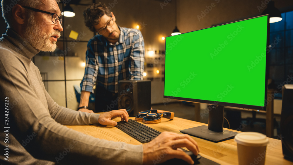 Poster in the evening creative middle aged man works on a desktop computer green mock-up screen, has conver
