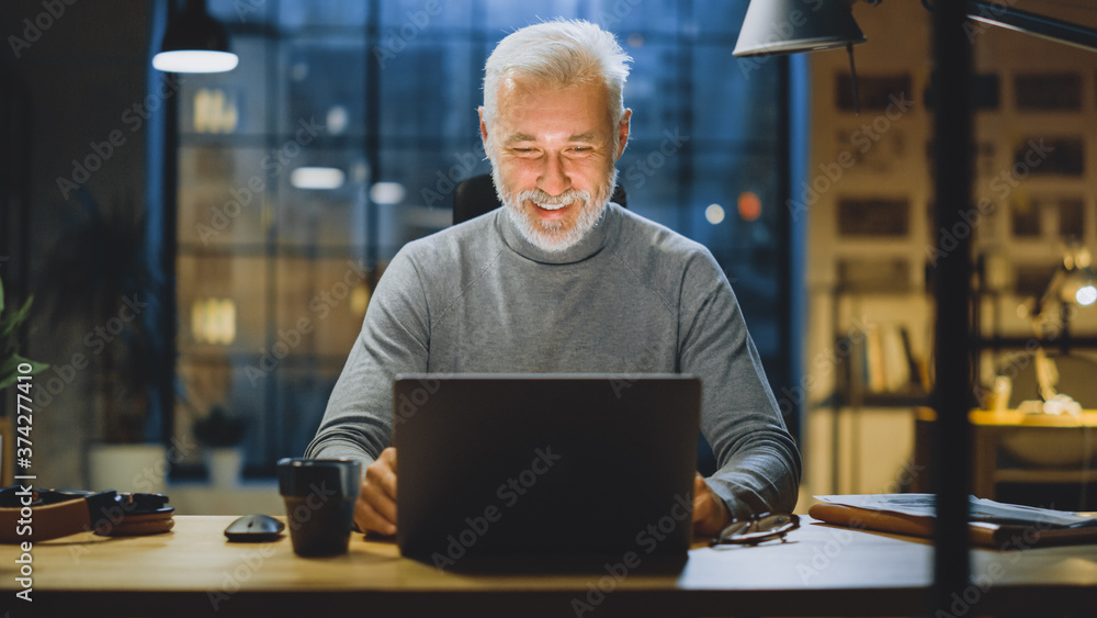 Poster portrait of the handsome smiling middle aged bearded businessman working at his desk using laptop co