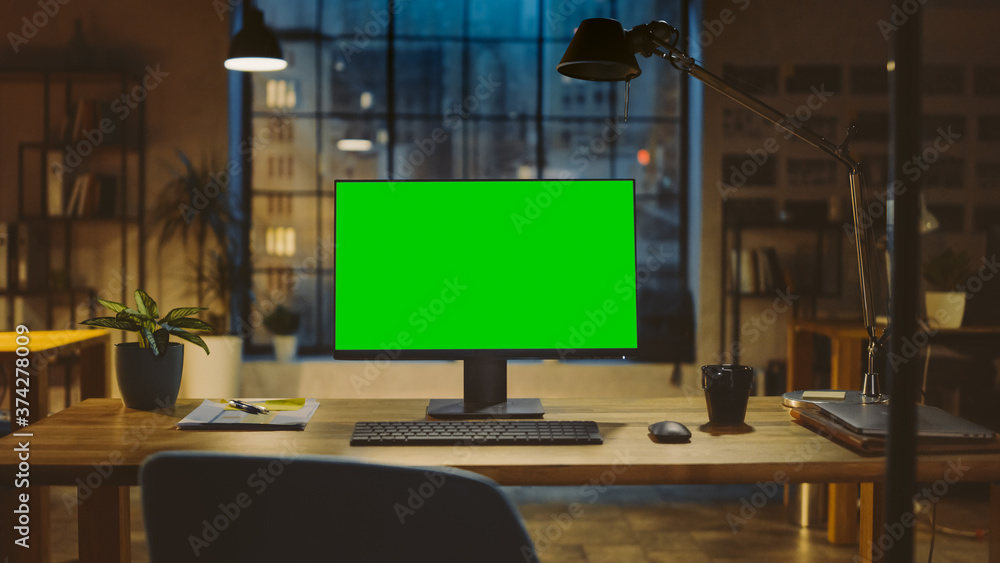 Poster Desktop Computer with Mock-up Green Screen Standing on the Wooden Desk in the Modern Creative Office. In the Background Warm Evening Lighting and Open Space Studio with City Window View.