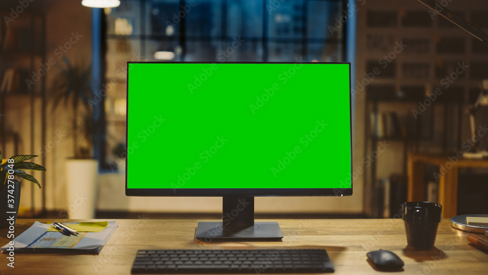 Poster Desktop Computer with Mock-up Green Screen Standing on the Wooden Desk in the Modern Creative Office. In the Background Warm Evening Lighting and Open Space Studio with City Window View.