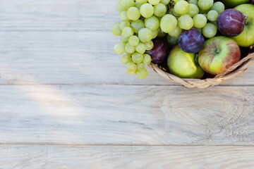 basket with grapes, apples and plums in the upper corner on a light wooden background