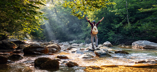 Happy male hiker trekking outdoors in forest near river