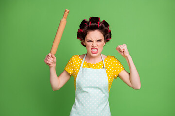 Photo of crazy evil furious lady curlers hairdo housewife hold rolling pin angry yell raise fist hate people step her kitchen wear pinup dotted dress apron isolated green color background
