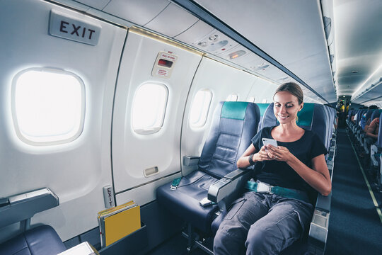 Travel And Technology. Young Woman In Plane Using Smartphone While Sitting In Airplane Seat.