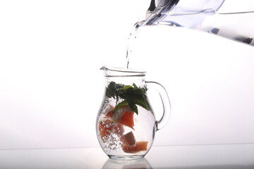 a carafe of water grapefruit and mint stands on a white background