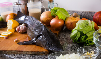 Whole fresh sturgeon lying on wooden cutting board with vegetables and spices on stone tabletop