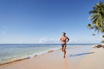 Fototapeta na wymiar Sports and healthy lifestyle. Young man jogging on the tropical beach.