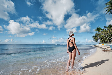 Vacation on the seashore. Back view of young woman walking away on the beautiful tropical white sand beach.