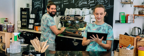 Coffee shop workers posing cleaning coffe maker and using tablet