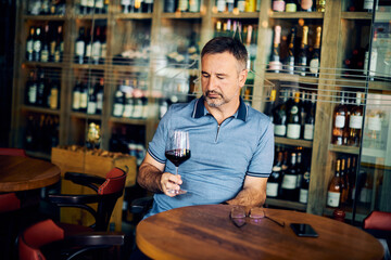 Mature adult wine taster sitting in winery and tasting wine.