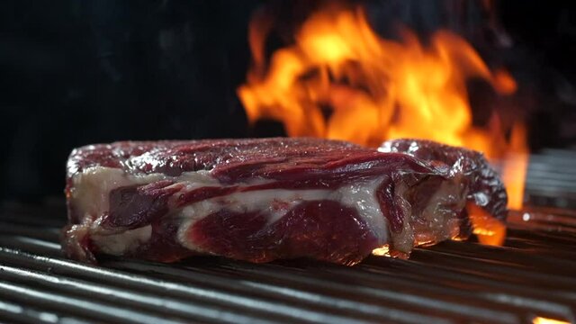 Raw beef steak falls on grill with burning fire and smoke.