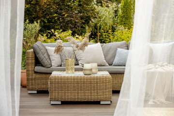 Lanterns, candles and vases on wicker coffee table in front of garden sofa
