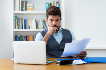 Concentrated working hispanic businessman with computer and paperwork
