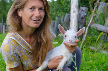 Woman with long hair and a small white kid goat. Countryside, farm, rural concept. People and animals.