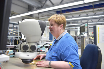 woman in a factory for the production of electronic components checks the quality of an assembled board with the help of a microscope or magnifying glass