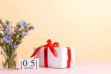 Flowers in a glass cup, gift and calendar with date of October 5, on a colored yellow pink...