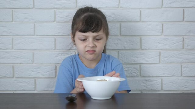 Eat porridge with mum. A little girl refuses a plate of porridge.
