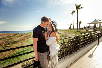Fototapeta premium Young man hugging his wife when they are standing near the beach promenade on summer day