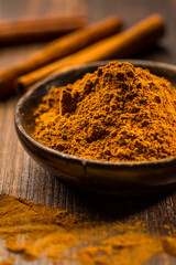 Cinnamon powder in wooden bowl with cinnamon sticks
