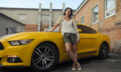 Young woman stands near yellow sport car.