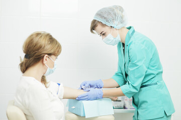 A female nurse in a medical mask takes a blood test from a patient.