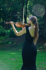 The girl plays the violin rear view. Violinist in a black dress in nature.
