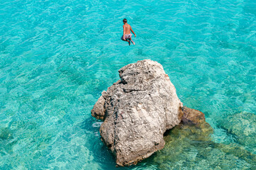 Lefkada, Greece. August 18th, 2011. A boy jumps from a rock into a turquoise sea in the bay of...