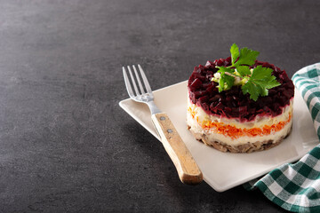 Traditional Russian herring salad with beetroot and carrots on black background.Copy space	