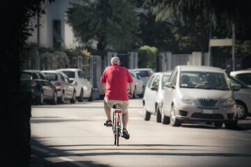 senior riding a bike in the traffic, man using bicycle but there are a lot of cars around him

