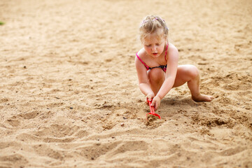 a small child plays in the sand. Beautiful girl sitting on the beach.