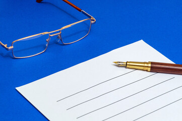 Blank for writing document with pen and glasses on a blue office desk