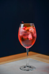 Citrus fruit cocktail in nice red color in front of a black background. Served in a wine glass on a wooden table.