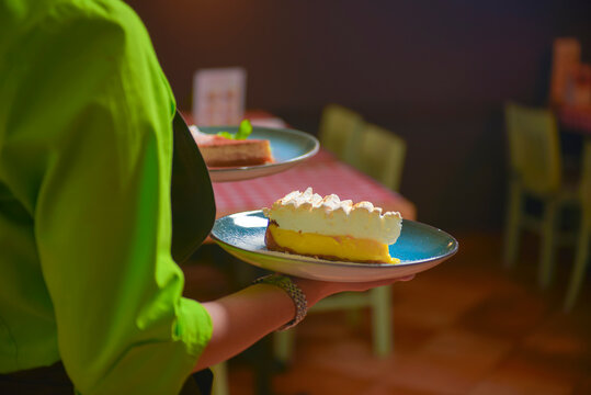 Waiter serves slice of lemon meringue pie in a blue plate. Delicious dessert. Eating out in restaurant.