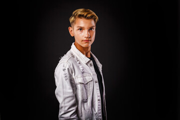 Fashion glamorous portrait of a handsome boy in white jacket on dark background.