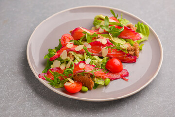 Fresh salad with smoked salted salmon, tomatoes and pumpkin seeds. Served on a gray plate over gray texture background.
