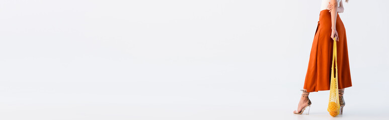 Fototapeta premium cropped view of woman in skirt posing with citrus fruits in yellow string bag isolated on white, panoramic shot