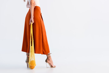 cropped view of woman in skirt posing with citrus fruits in yellow string bag isolated on white