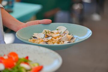 Waiter serving a meal in a restaurant. Salmon salad and pasta. Sea food concept. Eating out in restaurant.
