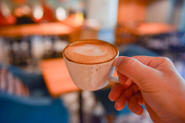 Male hand hold mug of espresso or americano coffee. Selected focus, blurred background. Inside of a restaurant or cafe.