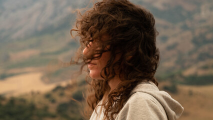 Woman with eyes closed and hair blown by the wind breathes deeply at the top of the mountain....