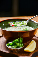 Popular spring and summer cold soup okroshka. Okroshka in a bowl, lemon and herbs on rustic wooden table.