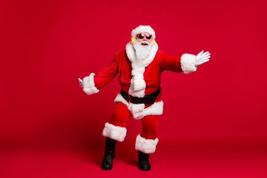 Full length x-mas photo of pensioner old man white beard plane dance newyear party wear santa costume gloves coat belt sunglass headwear earphones black boots isolated red color background
