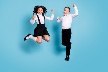 Full length photo of two opposite small girl boy schoolchildren brother sister classmates jump fists up last school day wear white shirt black pants dress isolated blue color background